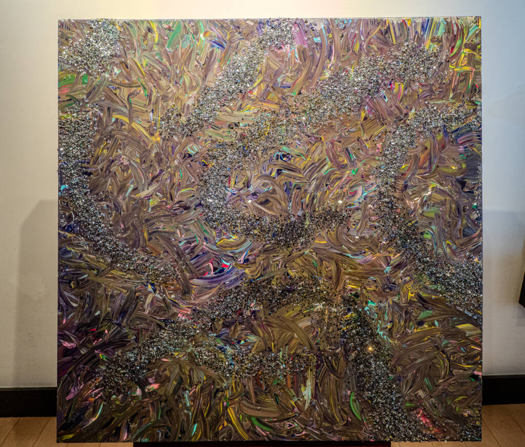 Abstract metallic painting with iridescent, swirling brushstrokes and silver glitter trails across a tall canvas in a gallery setting