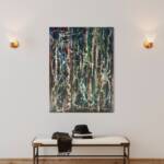 Abstract color-splattered painting on a light wall above a bench with a hat and scarf laid on a magazine-stacked table
