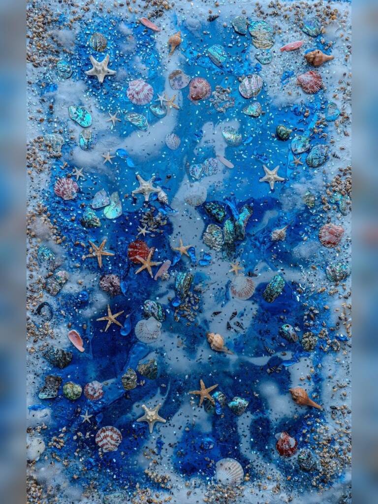 Blue-toned beach collage with assorted seashells, starfish, pebbles, and sand fragments scattered across a watery surface.